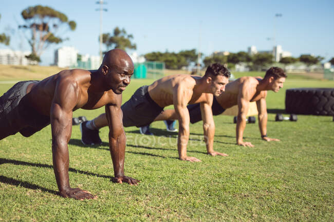 Разнообразная группа мускулистых мужчин, делающих отжимания упражнения на открытом воздухе. здоровый активный образ жизни, перекрестные тренировки для фитнеса. — стоковое фото