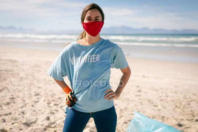Портрет женщины в футболках добровольцев и масках для лица, собирающей мусор. волонтеры по охране окружающей среды, уборка пляжа во время пандемии коронавируса 19. — стоковое фото