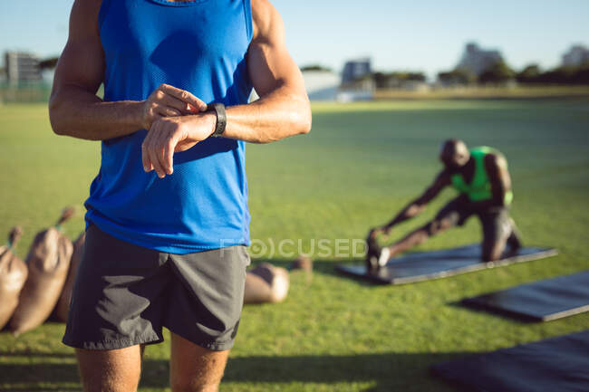 Sección media del hombre caucásico en forma haciendo ejercicio al aire libre, comprobando smartwatch. estilo de vida activo saludable, entrenamiento cruzado para fitness. - foto de stock
