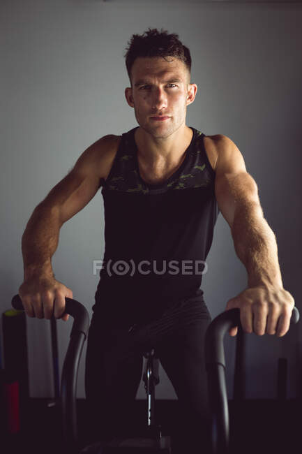 Retrato de hombre caucásico en forma haciendo ejercicio en el gimnasio, en bicicleta estática. estilo de vida activo saludable, entrenamiento cruzado para fitness. - foto de stock