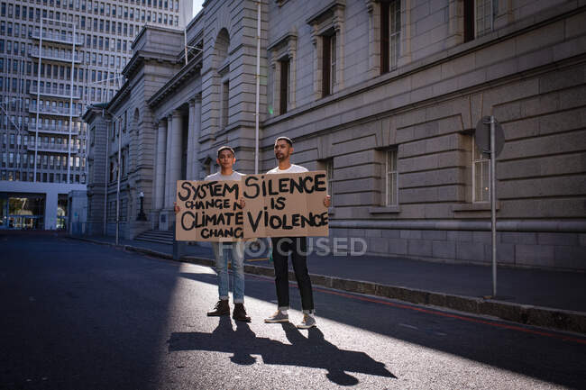 Deux amis de race mixte portant des panneaux de protestation peints à la main marchant dans la rue de la ville. Manifestants pour l'égalité des droits et la justice en ville. — Photo de stock