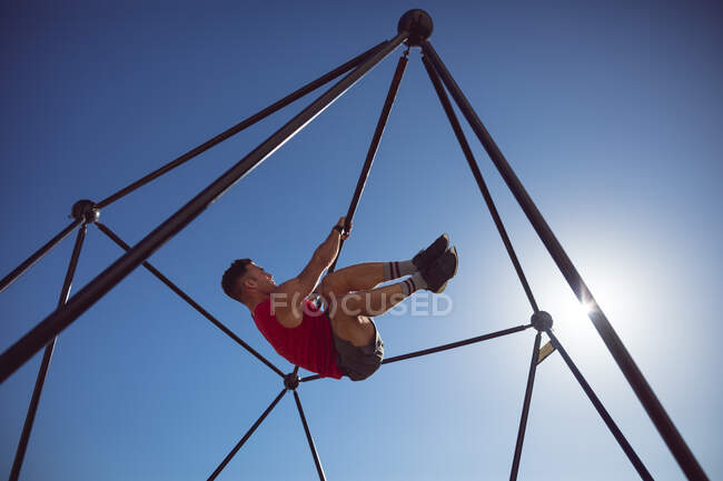 Кавказский мускулистый человек висит на тренировочной раме на открытом воздухе. здоровый активный образ жизни, кросс тренировки для фитнеса. — стоковое фото