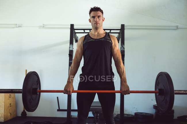 Retrato de hombre caucásico en forma haciendo ejercicio en el gimnasio, levantando pesas en la barra. estilo de vida activo saludable, entrenamiento cruzado para fitness. - foto de stock