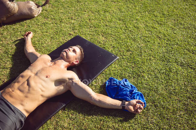 Homem musculoso caucasiano exercitando ao ar livre, deitado exausto na grama. estilo de vida ativo saudável, treinamento cruzado para fitness. — Fotografia de Stock
