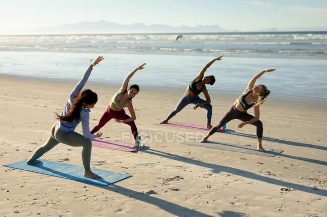 Groupe diversifié de femmes pratiquant le yoga, debout s'étirant à la plage. mode de vie sain et actif, forme physique extérieure et bien-être. — Photo de stock