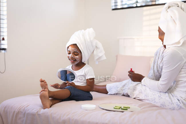 Счастливые африканские мама и дочь отдыхают в спальне, наслаждаясь косметическими процедурами. Семья проводит время вместе дома. — стоковое фото