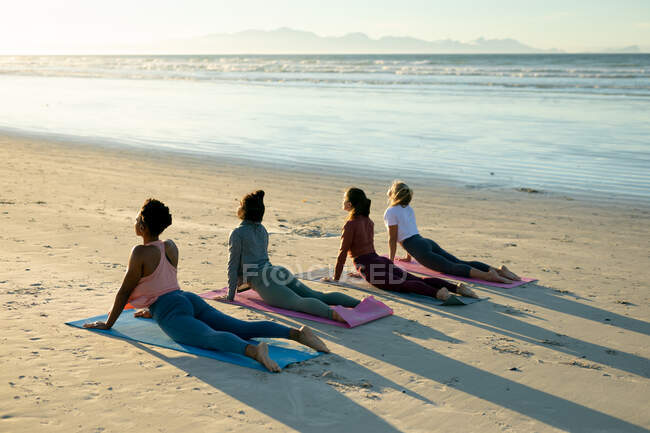 Gruppe verschiedener Freundinnen, die Yoga praktizieren, am Strand liegen und stärken. gesunder aktiver Lebensstil, Fitness und Wohlbefinden im Freien. — Stockfoto
