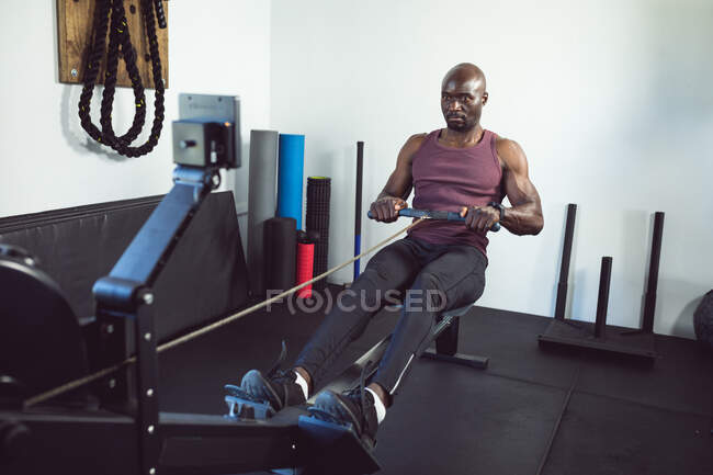 Подходящий африканский американец, тренирующийся в спортзале, используя тренажерку для гребли. здоровый активный образ жизни, кросс тренировки для фитнеса. — стоковое фото