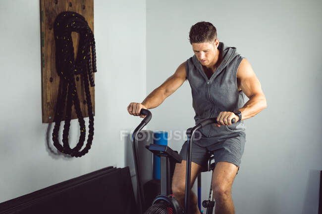 S'adapter homme caucasien faisant de l'exercice à la salle de gym, en utilisant vélo d'exercice. mode de vie sain et actif, entraînement croisé pour la forme physique. — Photo de stock