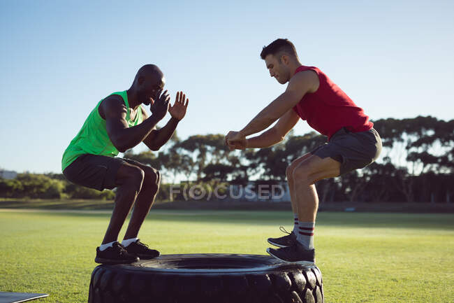 Zwei fitte Männer turnen im Freien und springen auf Traktorreifen. gesunder aktiver Lebensstil, Crosstraining für Fitness. — Stockfoto