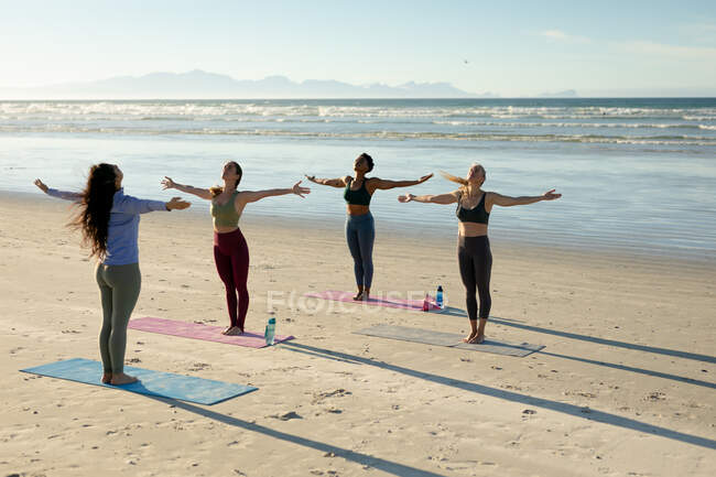 Diverse group of women practicing yoga practicing yoga, standing with arms outstretched at the beach. healthy active lifestyle, outdoor fitness and wellbeing. — Stock Photo