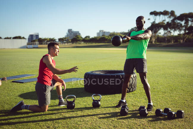 Diverse fit man and trainer exercising outdoors, instructing and swinging kettlebell weight. healthy active lifestyle, cross training for fitness. — Stock Photo