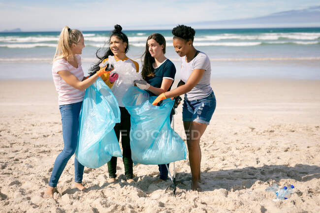 Diverse group of women walking along beach, picking up rubbish. eco conservation volunteers, beach clean-up. — Stock Photo