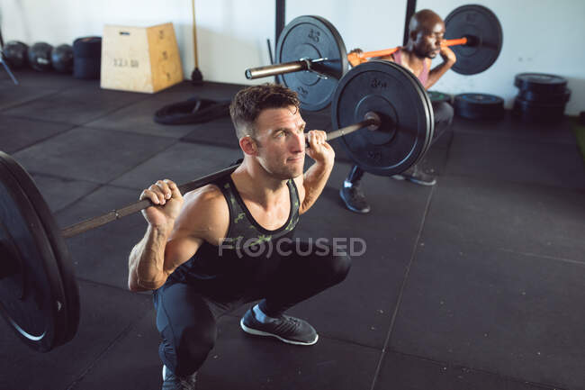 Ajustez l'homme caucasien exerçant à la salle de gym, soulevant des poids sur l'haltère. mode de vie sain et actif, entraînement croisé pour la forme physique. — Photo de stock