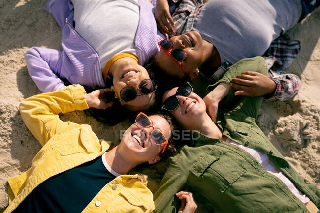 Fröhliche Gruppe unterschiedlicher Freundinnen, die sich amüsieren, Händchen haltend am Strand liegen und lachen. Urlaub, Freiheit und Freizeit im Freien. — Stockfoto