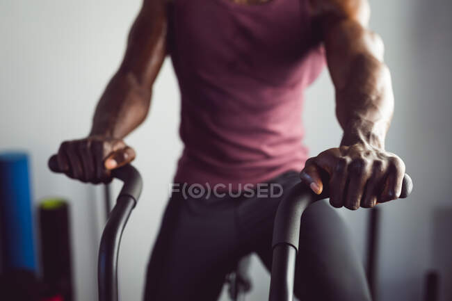 Sección media del hombre afroamericano ejercitándose en el gimnasio usando un remo. estilo de vida activo saludable, entrenamiento cruzado para fitness. - foto de stock