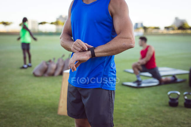 Midsection of fit man exercising outdoors, checking smartwatch. healthy active lifestyle, cross training for fitness. — Stock Photo
