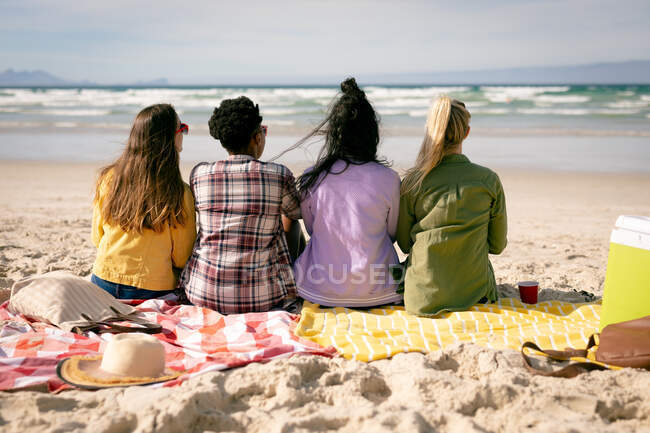 Fröhliche Gruppe unterschiedlicher Freundinnen, die Spaß haben, am Strand sitzen und das Meer betrachten. Freundinnen-Bonding am Strand. — Stockfoto