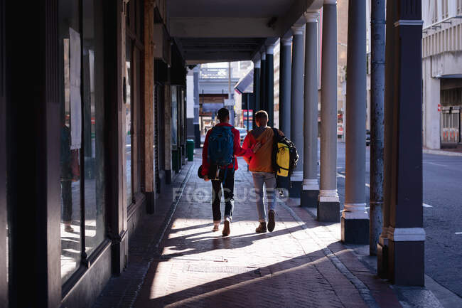 Вид ззаду на двох друзів-чоловіків, які носять рюкзаки, що ходять по вулиці міста. канікули в рюкзаку, перерва на проїзд по місту . — стокове фото