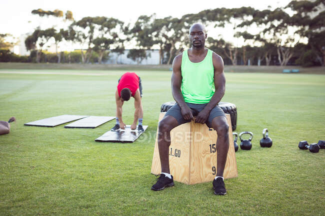 Retrato de homem afro-americano apto a se exercitar ao ar livre, fazer uma pausa, sentado na caixa. estilo de vida ativo saudável, treinamento cruzado para fitness. — Fotografia de Stock