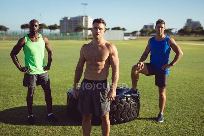 Retrato de un grupo diverso de hombres sin camisa que ejercen al aire libre junto a un neumático. estilo de vida activo saludable, entrenamiento cruzado para fitness. - foto de stock