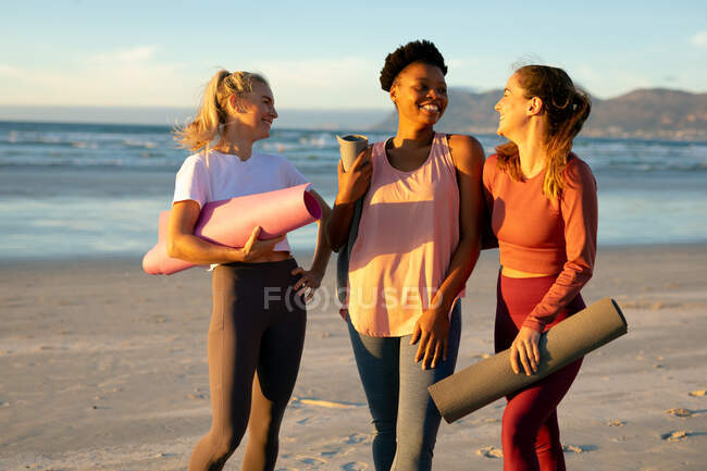 Группа счастливых разнообразных подруг практикующих йогу на пляже и отдыхающих. здоровый активный образ жизни, фитнес на открытом воздухе и благополучие. — стоковое фото