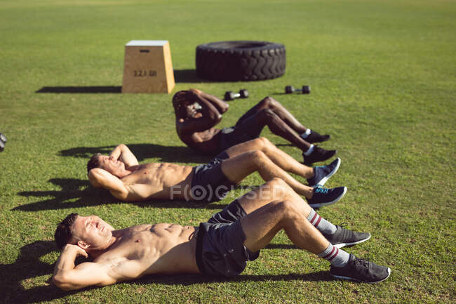 Diverso grupo de hombres musculosos haciendo crujidos haciendo ejercicio al aire libre. estilo de vida activo saludable, entrenamiento cruzado para el concepto de fitness. - foto de stock