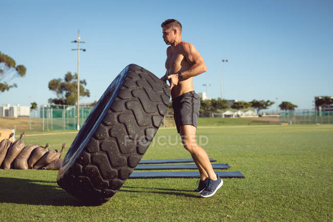 Uomo caucasico in forma senza maglietta che si allena all'aperto, sollevando pneumatici pesanti. sano stile di vita attivo, cross training per il fitness. — Foto stock