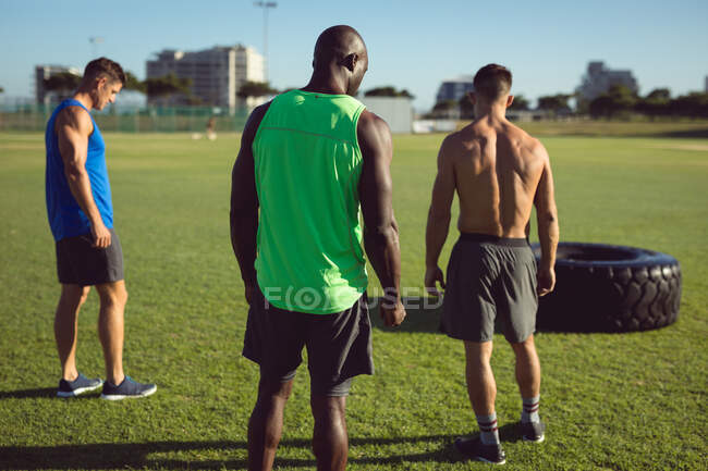 Three fit diverse men exercising outdoors, taking a break and catching their breath. healthy active lifestyle, cross training for fitness. — Stock Photo
