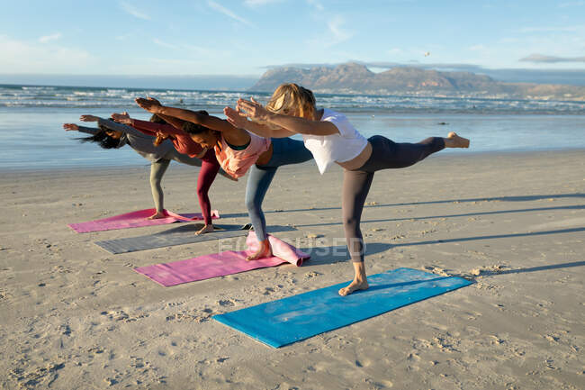 Group of diverse female friends practicing yoga, raising one leg stretching at the beach. healthy active lifestyle, outdoor fitness and wellbeing. — Stock Photo
