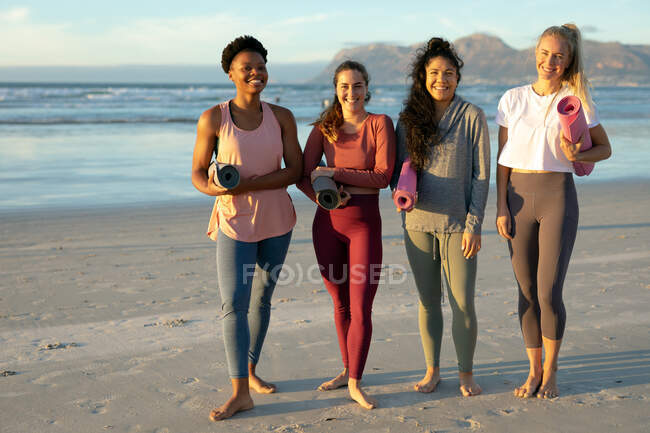 Groupe d'amis féminines diverses pratiquant le yoga, debout à la plage prendre une pause. mode de vie sain et actif, forme physique extérieure et bien-être. — Photo de stock