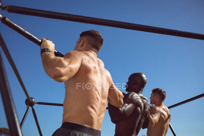 Diverso gruppo di uomini in forma senza maglietta che si esercitano all'aperto, facendo pull up sul telaio esercizio. sano stile di vita attivo, cross training per il fitness. — Foto stock
