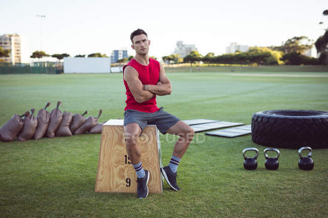 Porträt eines fitten kaukasischen Mannes, der im Freien trainiert, eine Pause einlegt und auf einer Loge sitzt. gesunder aktiver Lebensstil, Crosstraining für Fitness. — Stockfoto