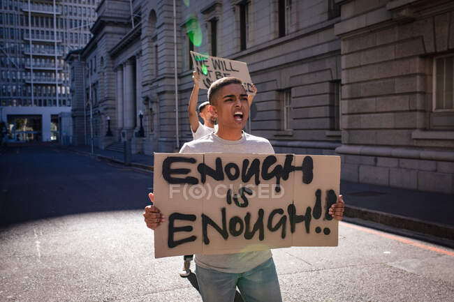 Zwei männliche Freunde gemischter Rassen tragen Protestschilder mit Parolen und schreien auf der sonnigen Straße der Stadt. Demonstranten für gleiche Rechte und Gerechtigkeit demonstrieren in der Stadt. — Stockfoto