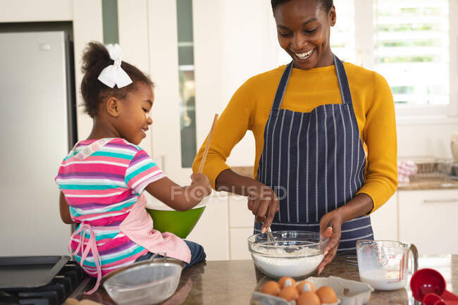 Улыбающиеся африканская американская мать и дочь веселятся на кухне, пекая вместе. Семья проводит время вместе дома. — стоковое фото