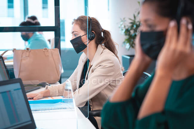 Group of diverse businesspeople wearing face mask using computer. work at a modern office during covid 19 coronavirus pandemic. — Stock Photo