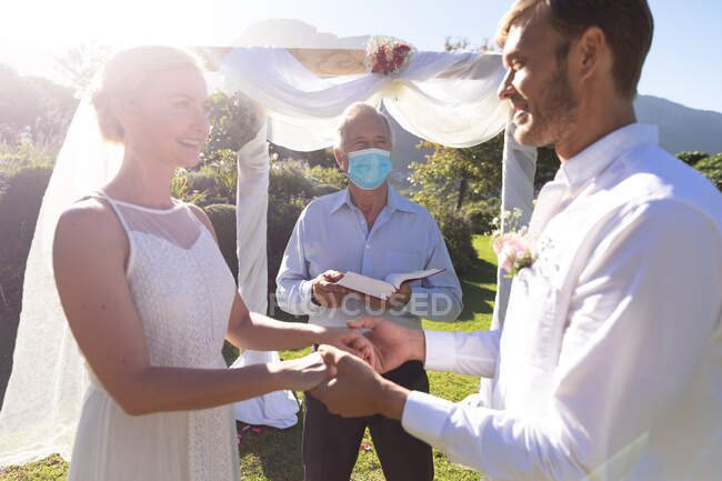 Felici sposi caucasici che si sposano tenendosi per mano giurando. matrimonio estivo, matrimonio, amore e celebrazione durante covid 19 concetto pandemico. — Foto stock