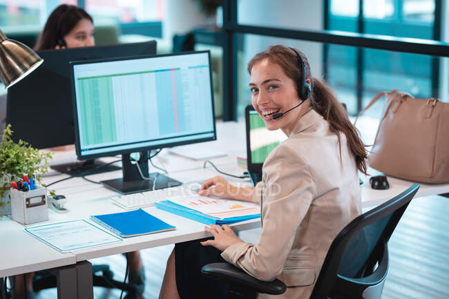 Portrait of caucasian businesswoman wearing headset and sitting at table smiling. work at a modern office. — Stock Photo