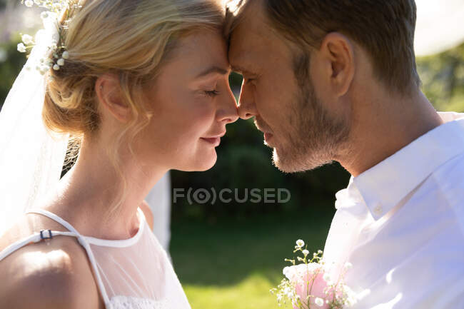 Glückliche kaukasische Braut und Bräutigam, die heiraten, berühren ihre Stirn. Sommerhochzeit, Ehe, Liebe und Festkonzept. — Stockfoto