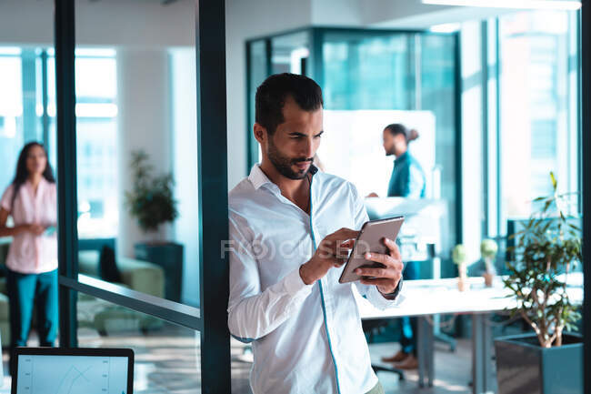 Gemischter Geschäftsmann mit Tablet und Kollegen im Hintergrund. Arbeit in einem modernen Büro. — Stockfoto