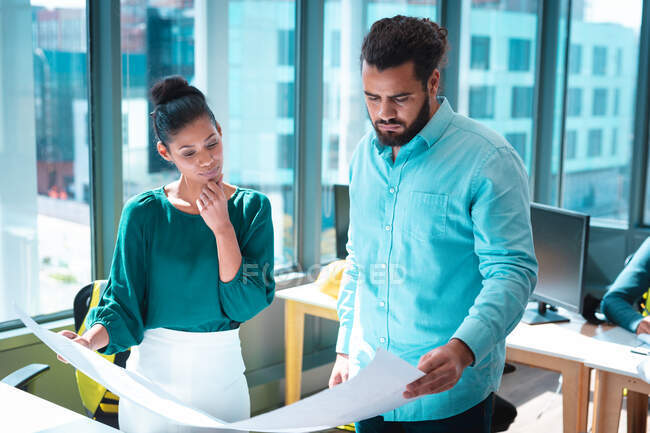 Zwei unterschiedliche Geschäftsleute diskutieren gemeinsam und halten einen Plan am Tisch. Arbeit in einem modernen Büro. — Stockfoto