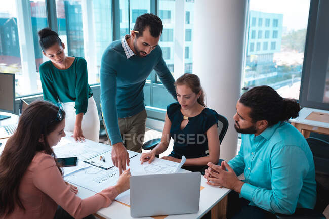 Группа различных бизнесменов обсуждают вместе, сидя за столом и используя ноутбук. работа в современном офисе. — стоковое фото