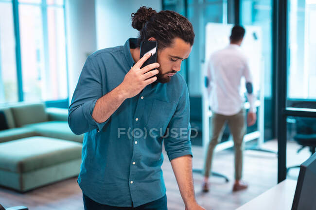 Homme d'affaires mixte utilisant un smartphone avec des collègues travaillant en arrière-plan. travailler dans un bureau moderne. — Photo de stock