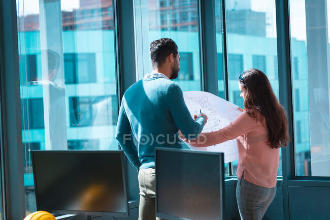 Dos empresarios diversos discutiendo juntos y sosteniendo esquema en ventana. trabajar en una oficina moderna. - foto de stock