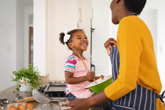 Sonriendo afroamericana madre e hija divirtiéndose en la cocina horneando juntas. familia pasar tiempo juntos en casa. - foto de stock