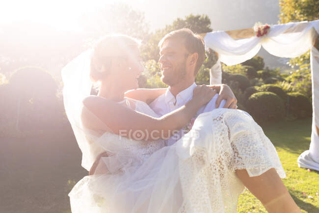 Glückliche kaukasische Braut und Bräutigam heiraten, Bräutigam trägt Braut. Sommerhochzeit, Ehe, Liebe und Festkonzept. — Stockfoto