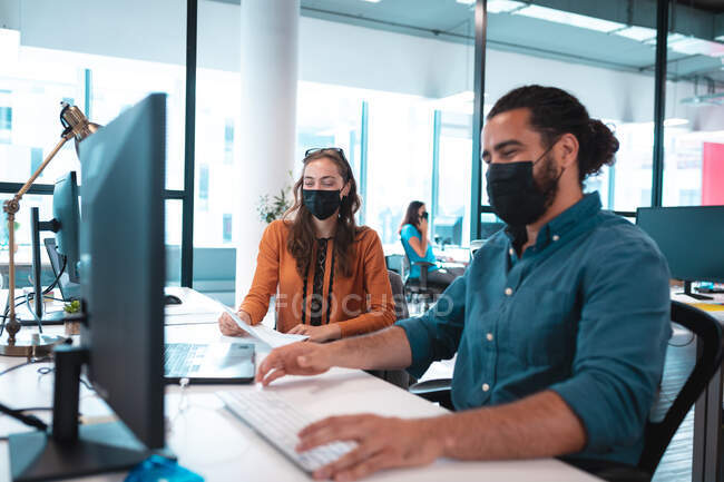 Dois empresários diversos usando máscara facial usando computador. trabalho em um escritório moderno durante covid 19 coronavirus pandemia. — Fotografia de Stock