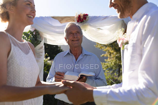 Feliz novia caucásica y novio casarse tomados de la mano jurando. boda de verano, matrimonio, amor y concepto de celebración. - foto de stock