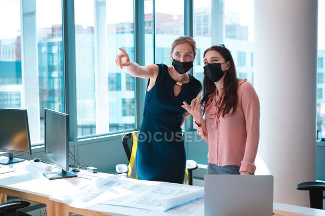 Two caucasian businesswomen wearing face mask and discussing. work at a modern office during covid 19 coronavirus pandemic. — Stock Photo