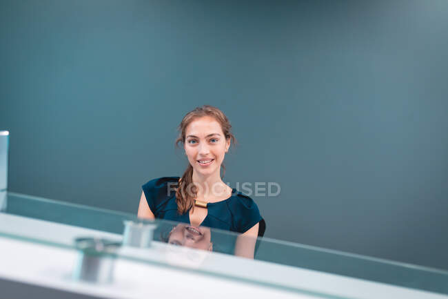 Retrato de una mujer de negocios caucásica sonriendo y sentada en una mesa de cristal. trabajar en un negocio creativo independiente. - foto de stock